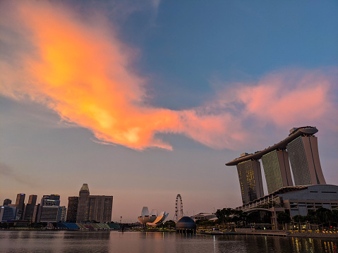 June 2020. Singapore. Panorama view of Marina bay Sands and the Marina district in Singapore at a late afternoon with the sunset light being reflected in the clouds. This photo was taken from the public path. The cloud formation is almost like the shape of a bird, eagle or a phoenix. Peaceful without any people, during the Singapore lockdown of 2020 because of the COVID-19 pandemic.