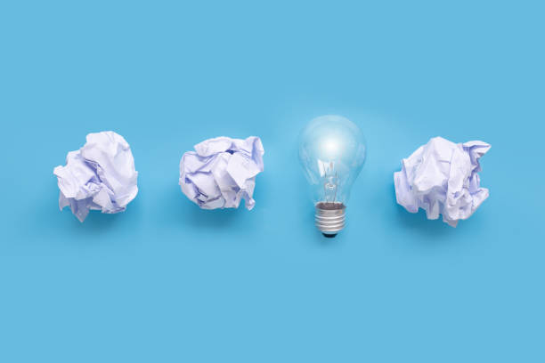 istock Light bulb  with white crumpled paper ball on blue background. 1251708604