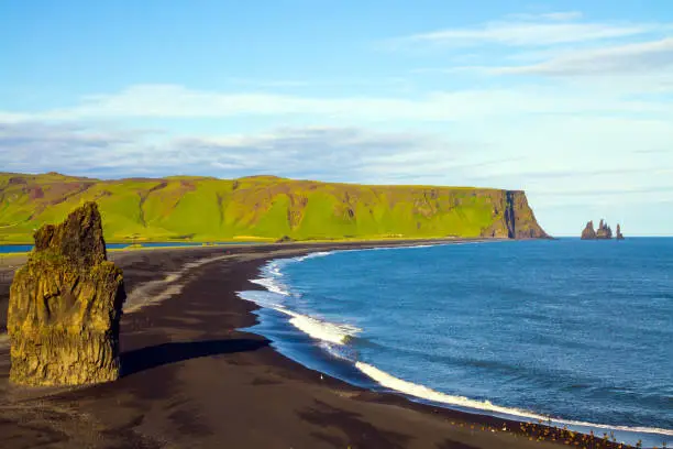 Travel to the fabulous island of Iceland. Giant lonely rock - Palm on a black volcanic sand beach Reinisfjara. Cape Dyrholaey. The concept of active, extreme and photo tourism