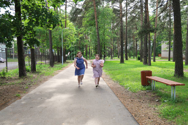 two little overweight joyful girls run along a path in a deserted park - mirth imagens e fotografias de stock