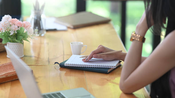 istock A woman is writing on a notebook while sitting at the wooden working desk. 1251716526