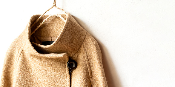 beige wool coat hanging on clothes hanger on white background.Close up.