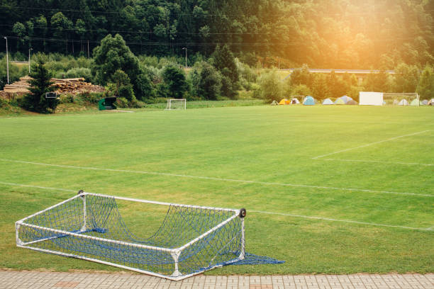 Fallen soccer football gate lying on empty green field with camping tents in the background