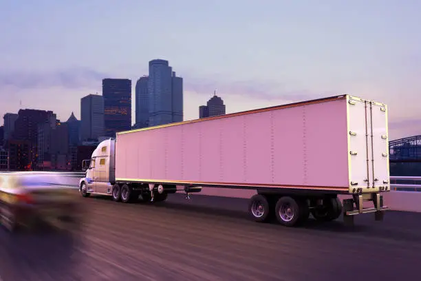 Photo of A cargo truck on the road at dusk in front of a city skyline.