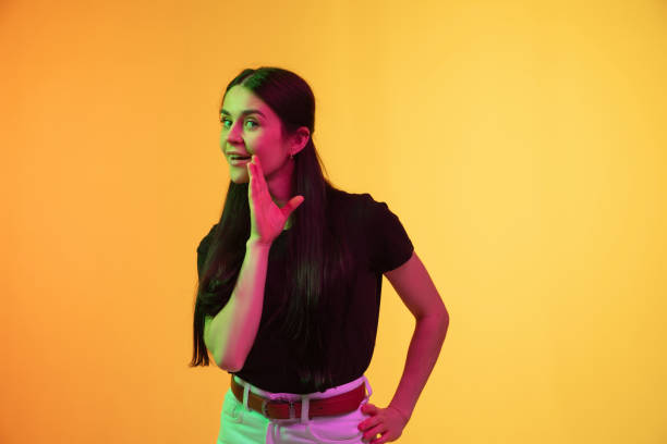 caucasian young woman's portrait on yellow background in neon light - neon orange imagens e fotografias de stock