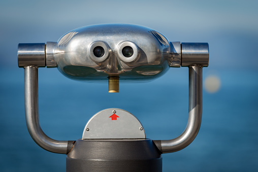 Close-up of a metallic coin operated binoculars for tourists on a blurred background, sea and sky