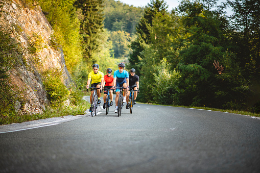 Front view of approaching male and female road bikers in 20s and 30s enjoying morning workout while climbing mountain road in rural area of Ljubljana.