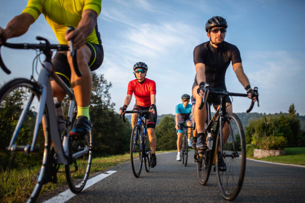 Group of Fit Cyclists Riding Mountain Road in Morning Low angle personal perspective of male and female road bike riders in 20s and 30s approaching and moving past camera during workout. racing bicycle photos stock pictures, royalty-free photos & images