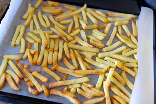 Roasted potato in shape of french fries made in the oven in baking pan on paper sheet, oil-free, fat-free