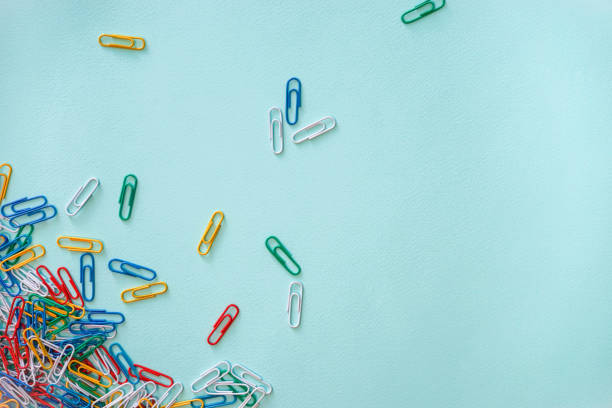istock Horizontal close-up flat lay composition of multi-colored paper clips on a light blue background. A pile of green, red, yellow, white and blue objects in the lower left corner. Part of the paper clips is located in the central and upper part of the image 1251728009