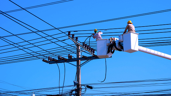 Two electricians on electric cable car are working to install power line against blue clear sky background in sunny day