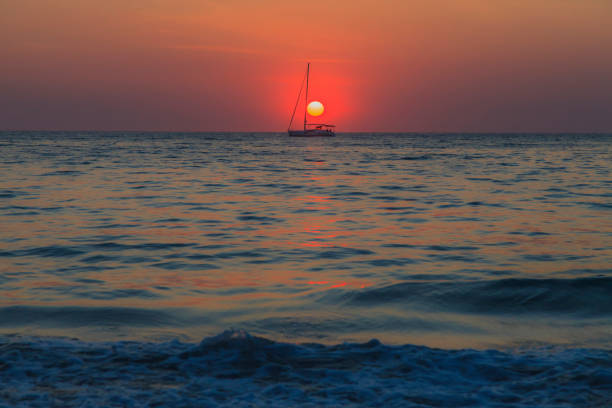 Photograph of a sunset over the sea with a sailing yacht in the backlight in Kamala Beach in November 2014