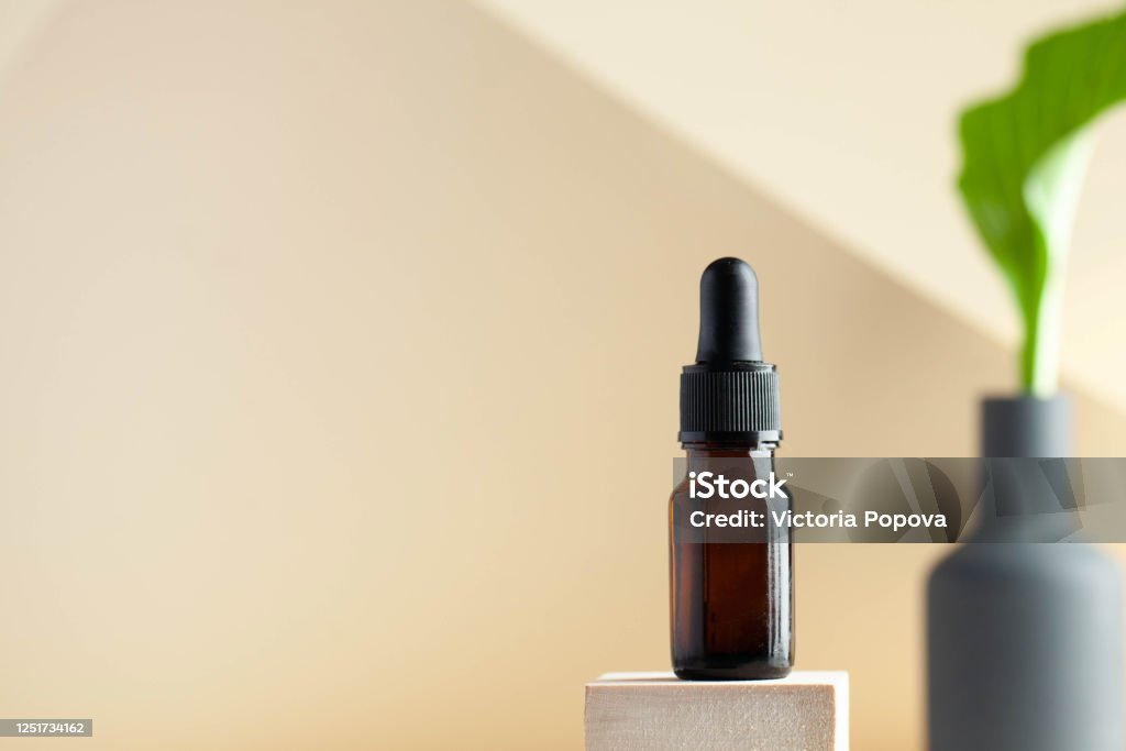 Serum oil for the face on a light background, with a place for text entry. Skin care. Copy space. Spa care concept Serum oil for the face in a dark glass flask on a light background, in the background is a green plant with a place to enter text from above. Skin care. Letter E Stock Photo