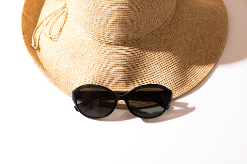 Beach straw hat with sunglasses on white.