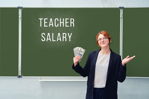 A woman holds us dollars at a blackboard with the text 