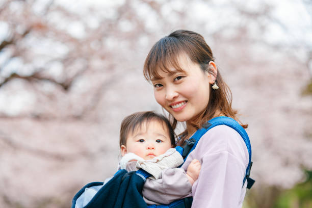 Mother embracing her small baby in front of cherry blossom tree A mother is embracing her small baby in front of a cherry blossom tree in a public park. carriage photos stock pictures, royalty-free photos & images