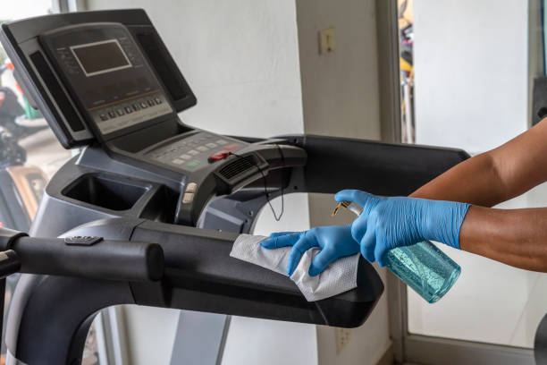 istock Staff using wet wipe and disinfectant from the bottle spraying a treadmill in gym. Antiseptic,disinfection ,cleanliness and healthcare. Anti bacterial and Corona virus COVID-19. 1251743473