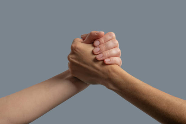 istock Close-up of light-skinned and dark-skinned people clasping hands 1251743753