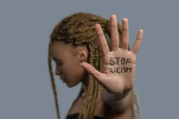 Photo of Young African American woman standing sideways, head down, showing palm with stop racism lettering