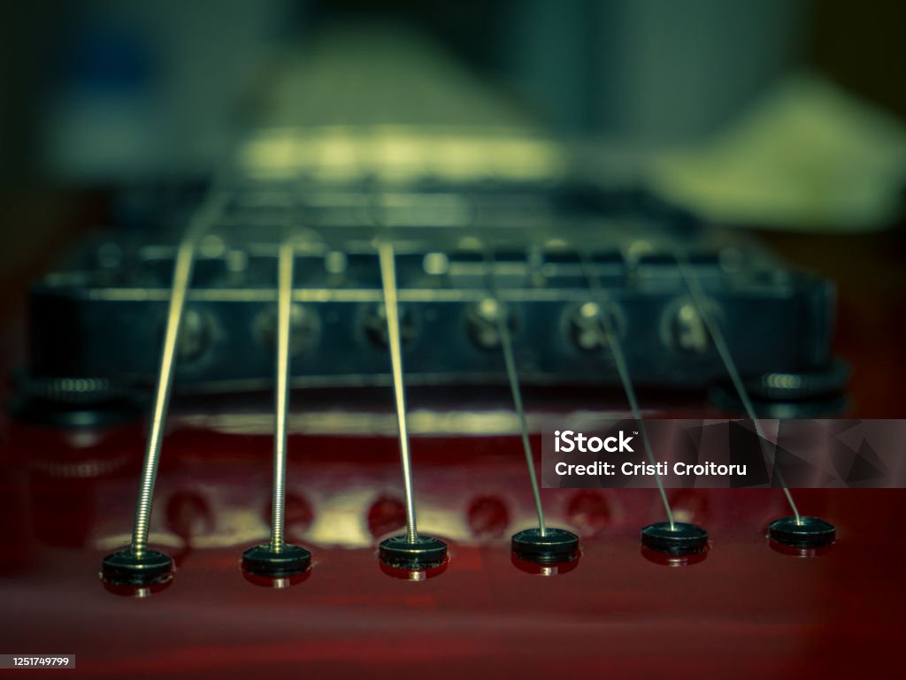 Close up with a guitar bridge and strings. Red guitar with blurred background. Audio Equipment Stock Photo