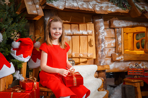 Little girl in a red dress with a Christmas present near a fabulous house