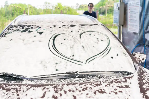 Photo of a heart is drawn on the car glass in foam at a car wash. the man in the background. symbol of respect for the car of the client