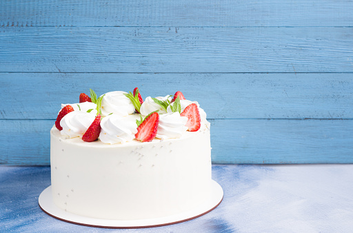 Beautiful white cake decoraited with meringue and fresh strawberries. Blue  background, copy space