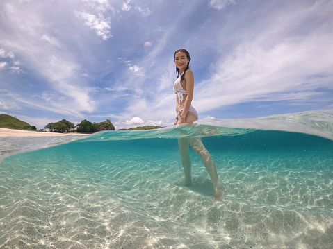 Half water view of woman in white bikini standing. pink sand at Komodo island, Indonesia.