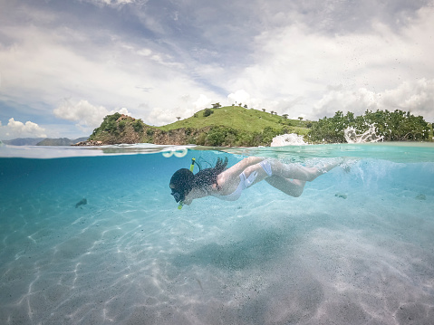 Half water view of woman in white bikini snorkeling. pink sand at Komodo island, Indonesia.