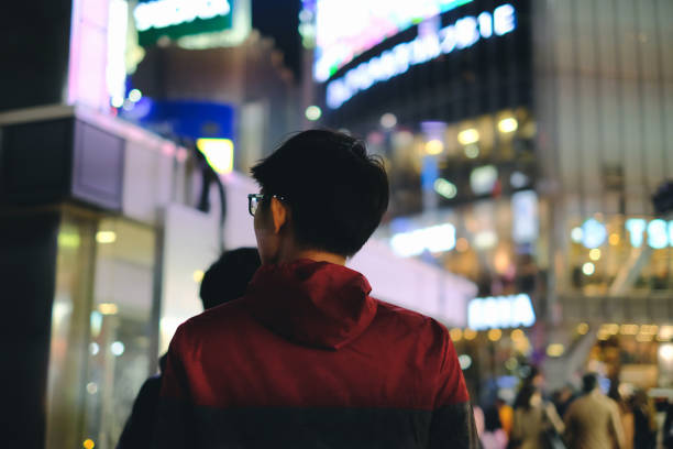 Young man walking in front of department store in big city with bokeh light background at night Young asian man walking in front of department store in big city with bokeh light background at night low angle street japan stock pictures, royalty-free photos & images