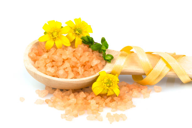 Macro view of wooden spoon with orange bath salt and autumn flowers isolated on white background