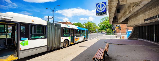 Panoramic view of Montreal Pie-IX metro station with double bus in front. Photographed during the Covid-19 epidemic, the station, bus and street are eerily empty. Bus back doors are open to let commuters in as preventative measure.