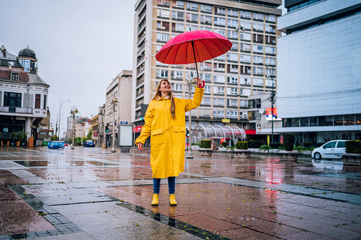 Cheerful young woman under red umbrella in the rain at the city