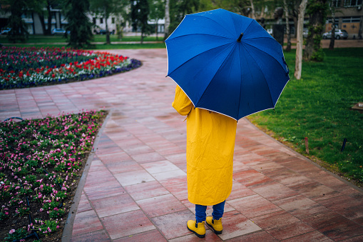 Young woman with blue umbrella standing in the rain at the park