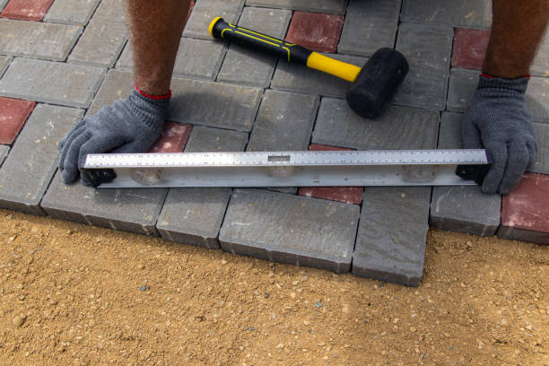 A craftsman in gloves with a rubber mallet lays concrete blocks on a gravelly sand base. Laying concrete blocks on the sidewalk. un artesano enguancido está colocando baldosas de hormigón usando un nivel de burbuja y un mazo de goma. sonidos de colocación de azulejos. pasarela de ladrillo pavimentada con pavimentadora profesional. colocación de losas de pavimento de hormigón gr