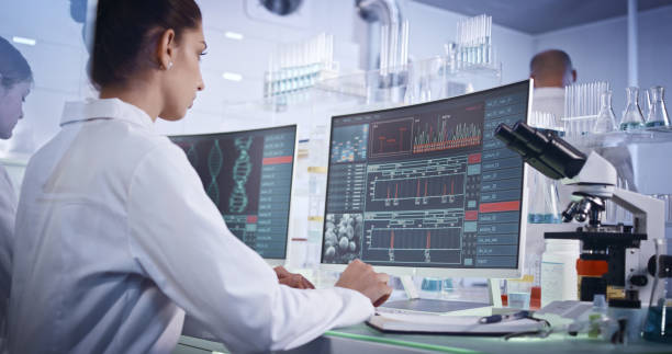 istock Research team studying DNA mutations. Computer screens with DNA helix in foreground 1251892304