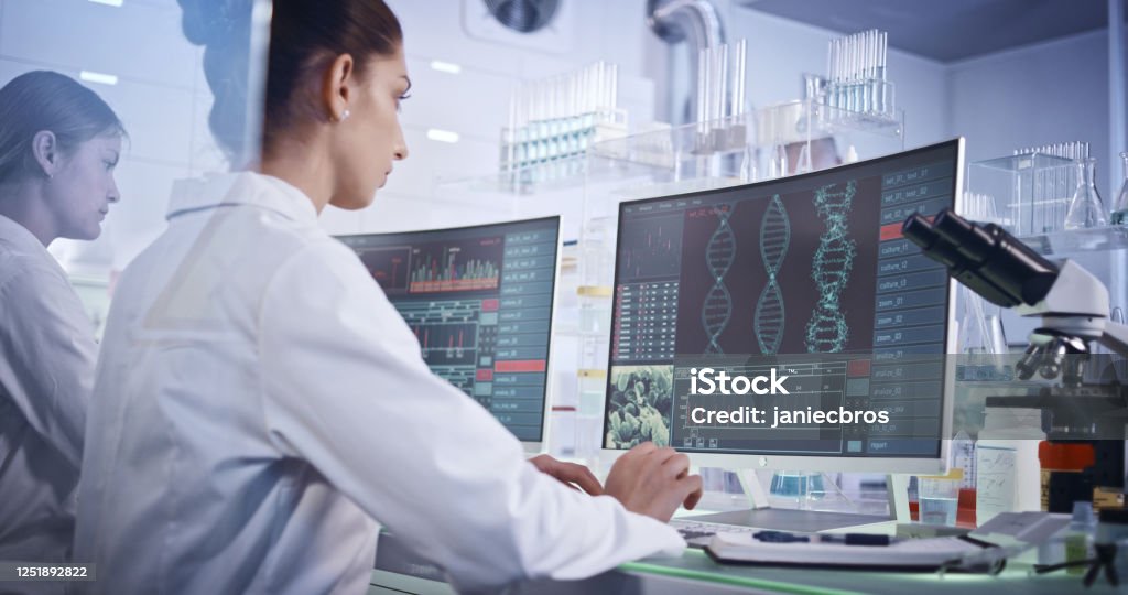 Weibliches Forschungsteam untersucht DNA-Mutationen. Computerbildschirme mit DNA-Helix im Vordergrund - Lizenzfrei DNA Stock-Foto