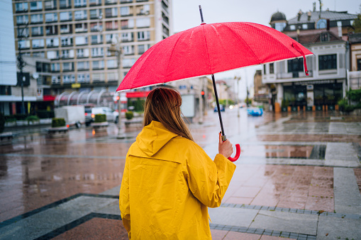 Woman with a red umbrella standing in the rain at the city