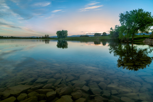 Trees reflect in the lake with rocks in the foreground on a spring morning