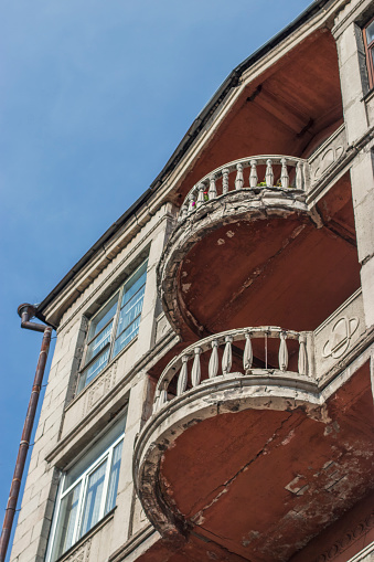 Two dilapidated balconies on a building of the twentieth century with flowers on a bright sunny day in summer against a blue sky. A walk through the old city in the Russian province.