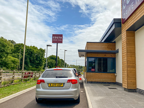Talbot Green, Wales - June 2020: Cars waiting to pick up orders from the window of a drive thru service facility of a Costa Coffee store. Costa is a British coffeehouse chain which is now a subsidiary of The Coca-Cola Company.