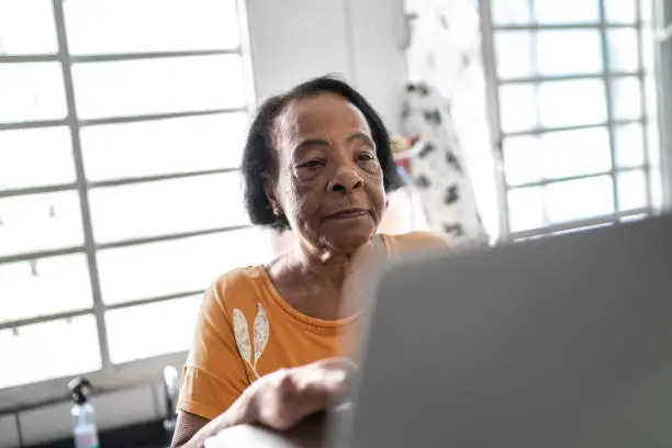 Senior woman using laptop and writing some notes at home