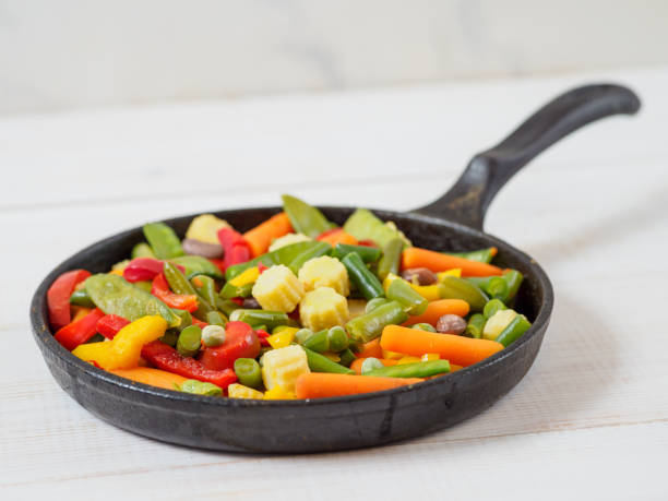 Fresh vegetables fried in the pan. White wooden background and space for text.