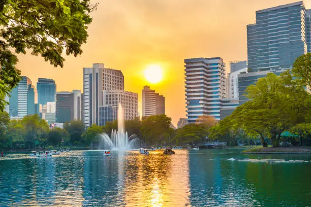 Scenic view of Lumphini park with beautiful lake with fountain and skyscrapers buildings on skyline at sunset. Bangkok city, Thailand