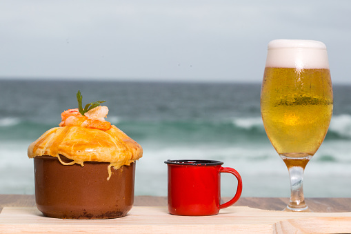 Brazilian snack. pie with shrimp with glass of beer with the beach in the background. In Brazil called empada or empadão