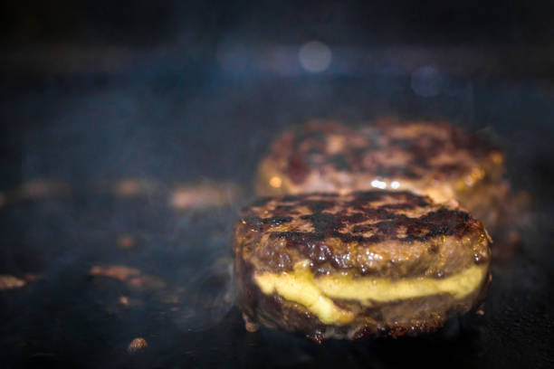 burger meat on hot iron plate grilling stuffed with melting cheese.