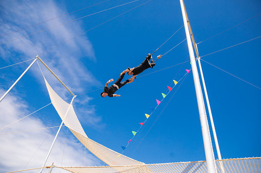 Two trapeze artists connected and swinging together in the sky