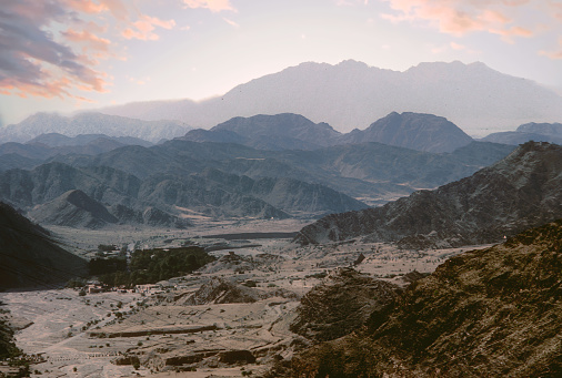Pale peach of dawn with morning mist obscuring the furthest range of mountains, while the others in mid and foreground are in stark relief.  The romance and wild, exotic nature of the Khyber pass, with no one in sight.