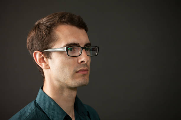 close-up studio portrait of a 28 year old man with glasses in a blue shirt on a black background