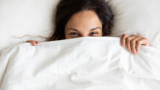 istock Smiling young woman hide under blanket waking up 1252119996